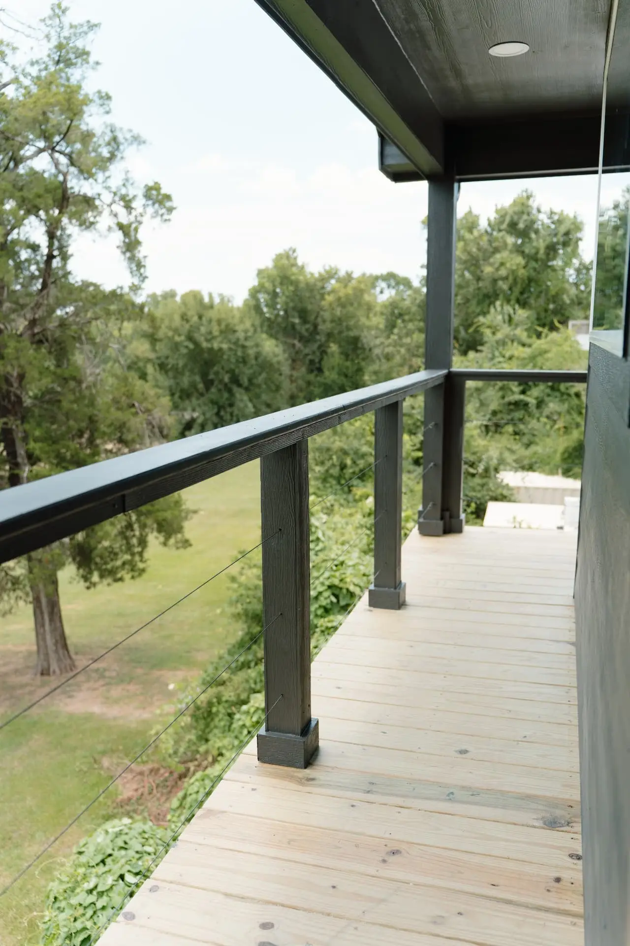 Covered upper balcony with cable railing overlooking trees